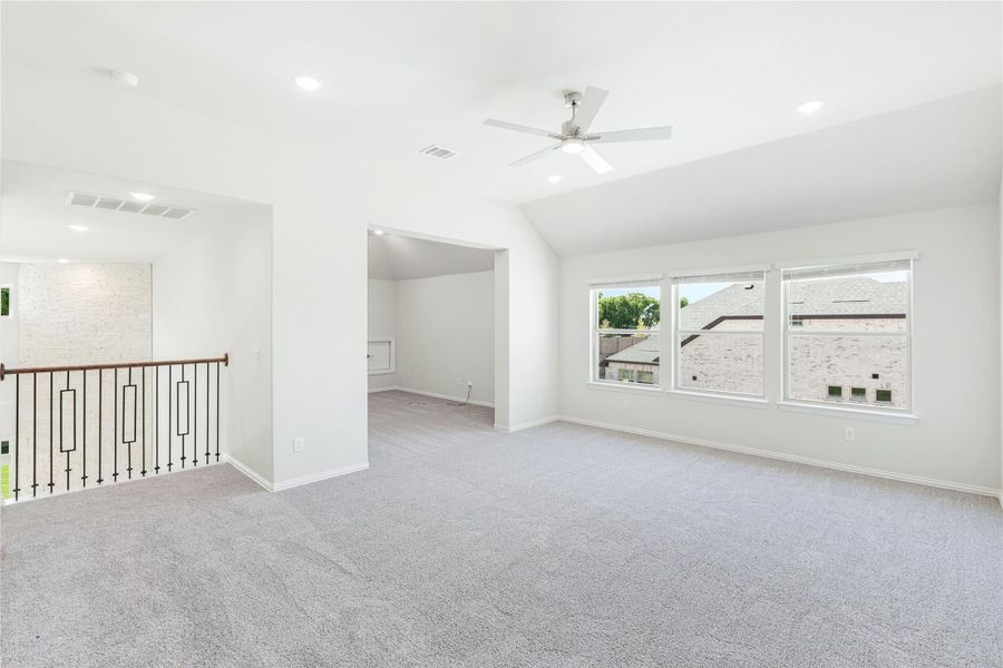 Spacious upstairs bonus room with gray carpet, ceiling fan, vaulted ceiling, and staircase railing