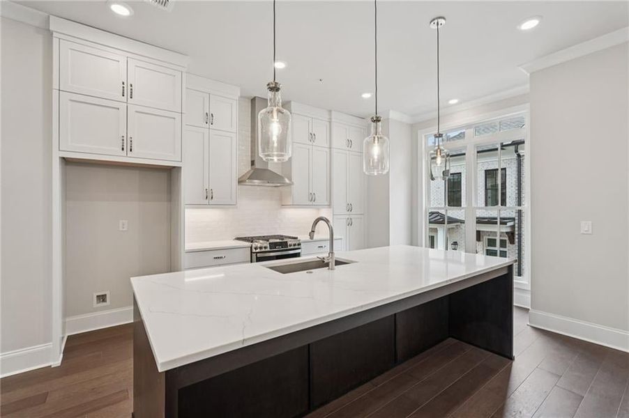 Dual tone kitchen with ornamental molding, hanging light fixtures, decorative backsplash, stainless steel range with gas cooktop, and dark wood-style floors
