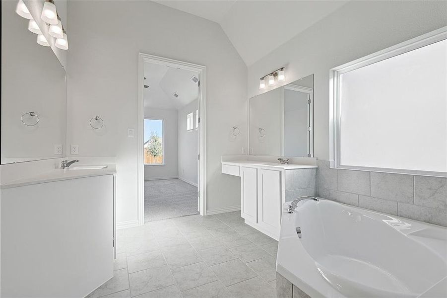 Bathroom featuring tiled tub, tile patterned flooring, vanity, and lofted ceiling