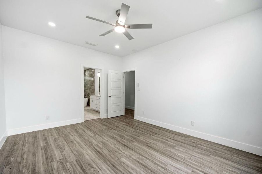 Spacious room featuring wood-finish flooring, white walls, and an overhead ceiling fan Spacious room featuring wood-finish flooring, white walls, and an overhead ceiling fan