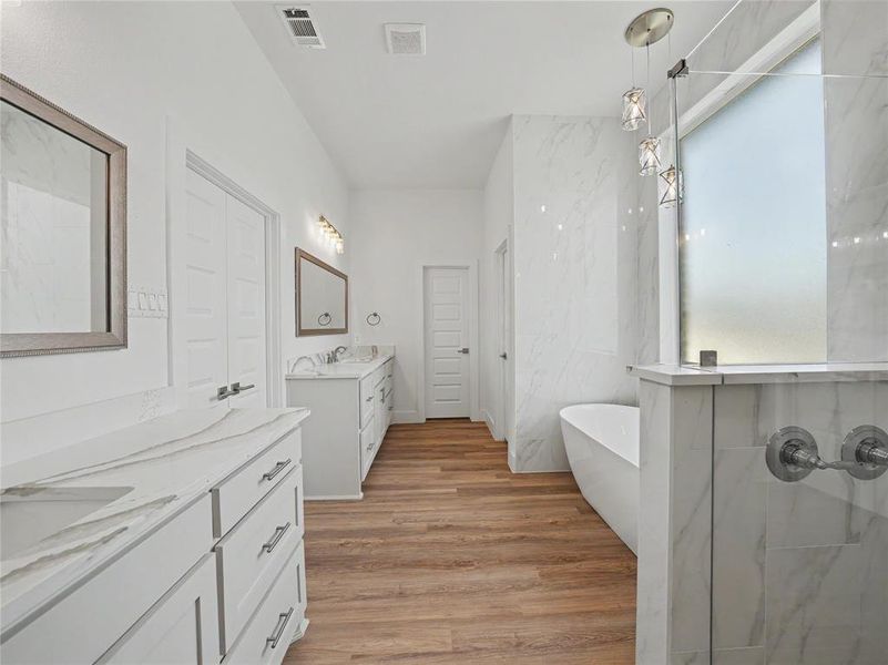 Contemporary bathroom featuring a freestanding tub, a walk-in shower with a frosted glass panel, and dual vanities with white cabinetry and light-toned countertops