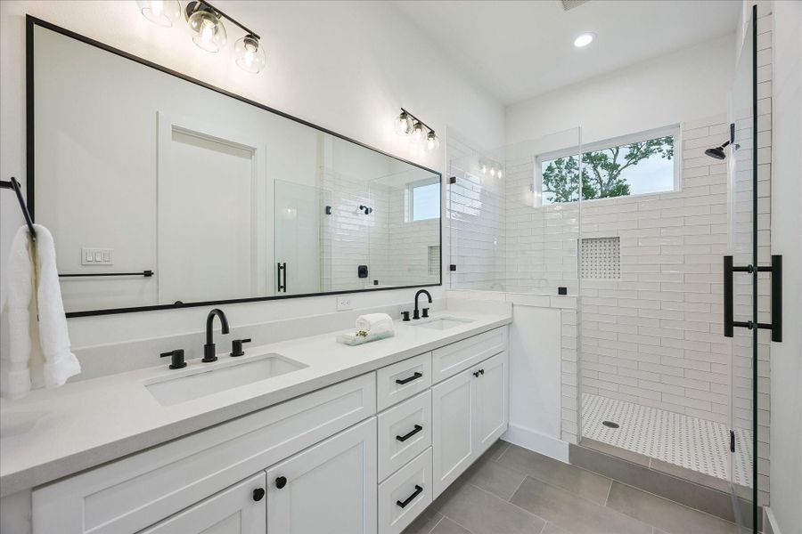 The spa-inspired primary bath features dual vanities and a spacious walk-in shower with a built-in bench. Designer tilework and a convenient shampoo niche add the perfect finishing touches. The spa-inspired primary bath features dual vanities and a spacious walk-in shower with a built-in bench. Designer tilework and a convenient shampoo niche add the perfect finishing touches.