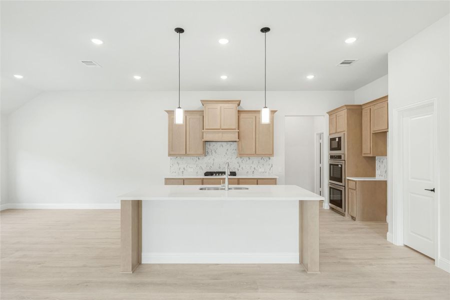 Open kitchen with large center island, light wood cabinets, marble backsplash, and pendant lights over white countertops