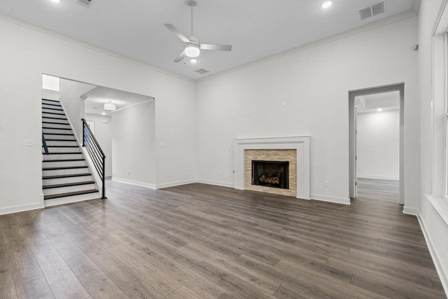 Unfurnished living room with stairway, a ceiling fan, wood finished floors, a fireplace, and crown molding
