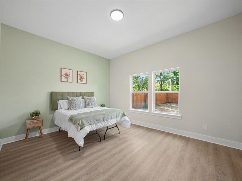 Spacious room featuring wood-finish flooring, a contemporary ceiling light fixture, and a light green accent wall Spacious room featuring wood-finish flooring, a contemporary ceiling light fixture, and a light green accent wall