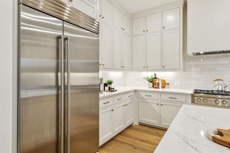 Kitchen featuring white cabinetry, light stone counters, built in refrigerator, light wood-type flooring, and decorative backsplash