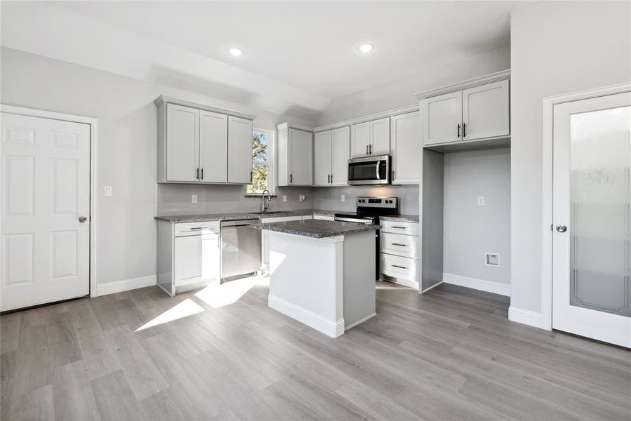 Kitchen with a center island, lofted ceiling, dark stone countertops, light wood-type flooring, and appliances with stainless steel finishes