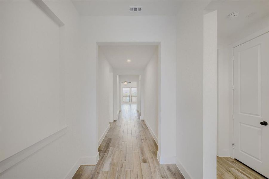 Hallway with wood-finish flooring extending into the background, bright white walls, recessed ceiling lighting, and a paneled door with dark hardware