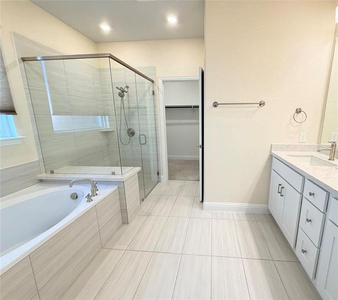 Full bath featuring vanity, a shower stall, a garden tub, a walk in closet, and light tile patterned flooring Full bath featuring vanity, a shower stall, a garden tub, a walk in closet, and light tile patterned flooring