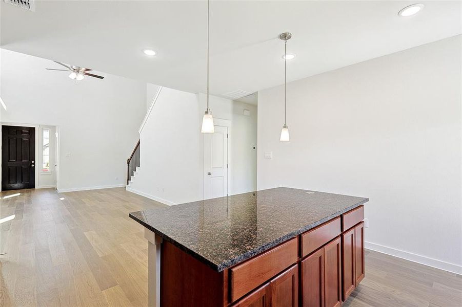 Kitchen featuring pendant lighting, light wood-type flooring, a center island, dark stone countertops, and ceiling fan