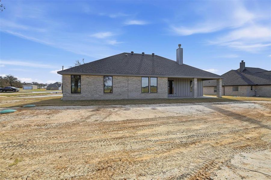 Back of house with a patio, brick siding, roof with shingles, and a chimney