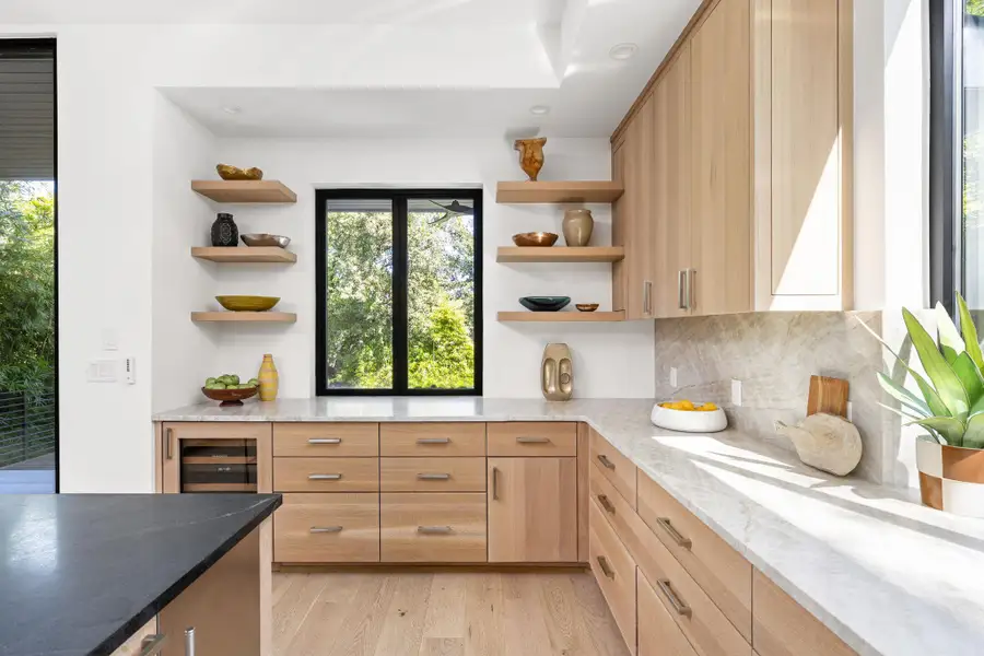 Kitchen featuring light brown cabinets, open shelves, dark stone counters, light wood finished floors, and beverage cooler Kitchen featuring light brown cabinets, open shelves, dark stone counters, light wood finished floors, and beverage cooler