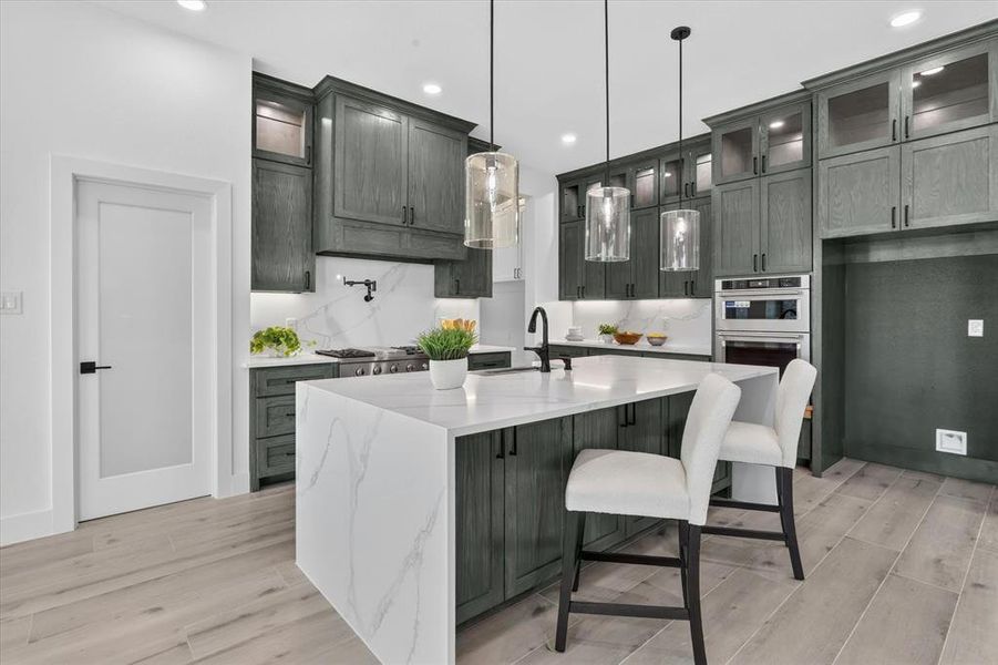 Kitchen featuring a waterfall island with a white countertop and seating, gray wood-finish cabinetry, stainless steel appliances, and wood-finish flooring