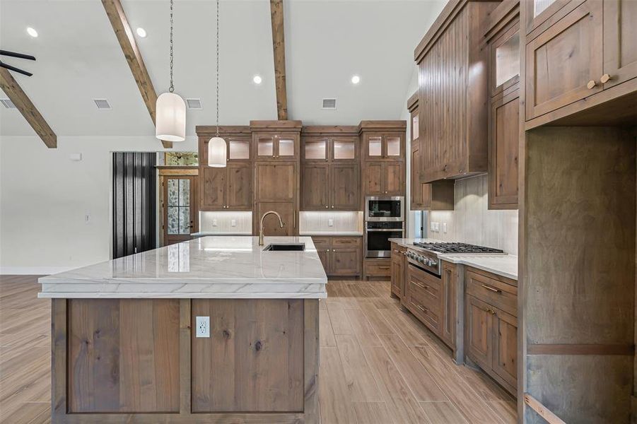 Kitchen featuring brown cabinetry, decorative backsplash, appliances with stainless steel finishes, glass insert cabinets, and pendant lighting Kitchen featuring brown cabinetry, decorative backsplash, appliances with stainless steel finishes, glass insert cabinets, and pendant lighting