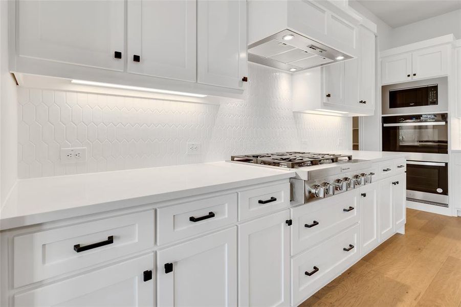 Kitchen with light hardwood / wood-style flooring, exhaust hood, tasteful backsplash, white cabinetry, and appliances with stainless steel finishes