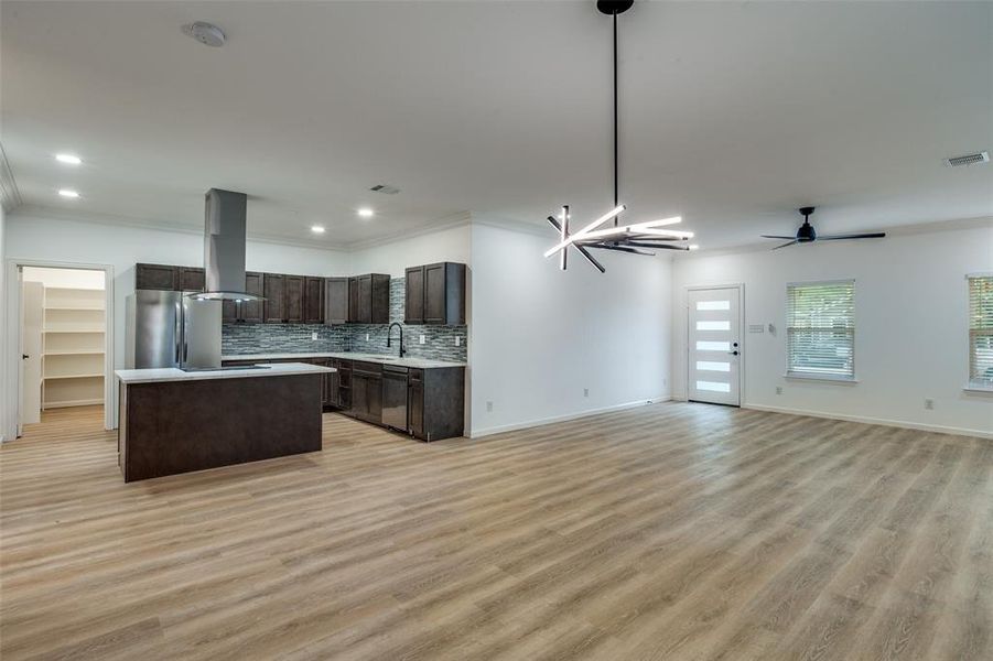 Kitchen featuring open floor plan, ornamental molding, dark brown cabinetry, a center island, and light countertops Kitchen featuring open floor plan, ornamental molding, dark brown cabinetry, a center island, and light countertops