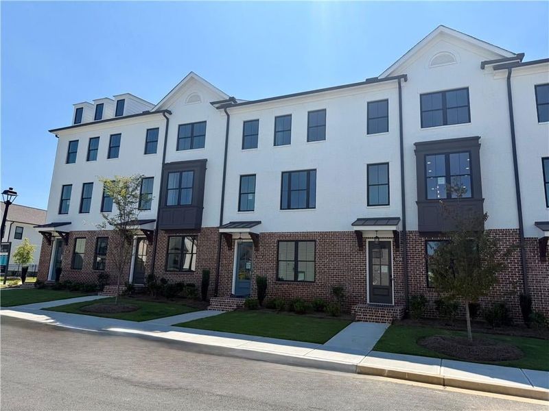 Modern townhome exterior featuring white painted brick, a dark framed bay window, dark window frames, and a brick facade Modern townhome exterior featuring white painted brick, a dark framed bay window, dark window frames, and a brick facade