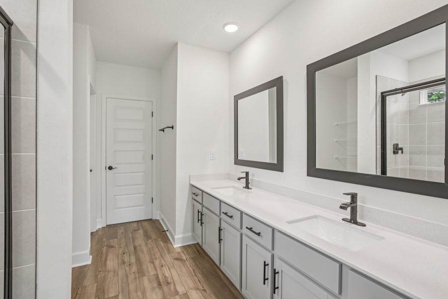 Sophisticated dual sinks and dark framed mirrors complement rich wood flooring in Spring Hill's elite locale.