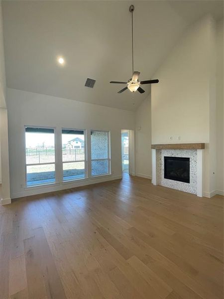 Unfurnished living room with a glass covered fireplace, a ceiling fan, vaulted ceiling, and light wood-style floors