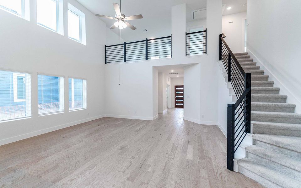 Unfurnished living room with a ceiling fan, light wood-style floors, and a high ceiling Unfurnished living room with a ceiling fan, light wood-style floors, and a high ceiling