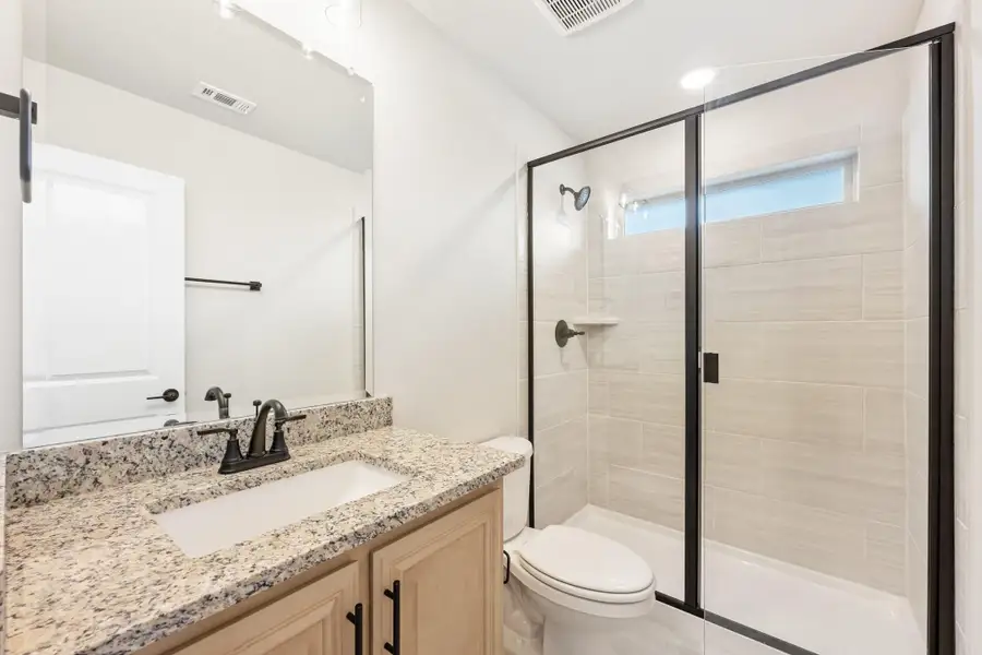Bathroom with granite vanity, glass-enclosed tiled shower, and wood cabinets with black hardware Bathroom with granite vanity, glass-enclosed tiled shower, and wood cabinets with black hardware