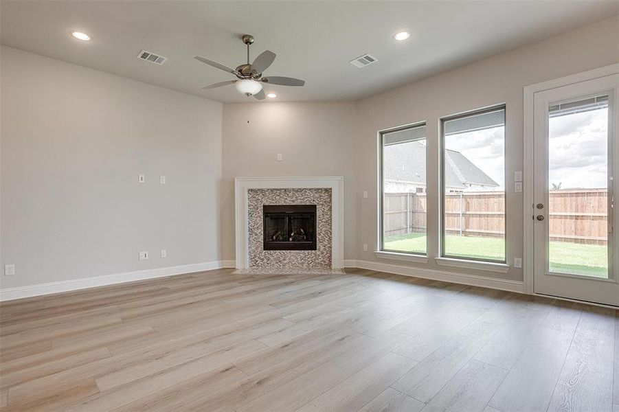 Unfurnished living room with a tiled fireplace, light wood-type flooring, and ceiling fan