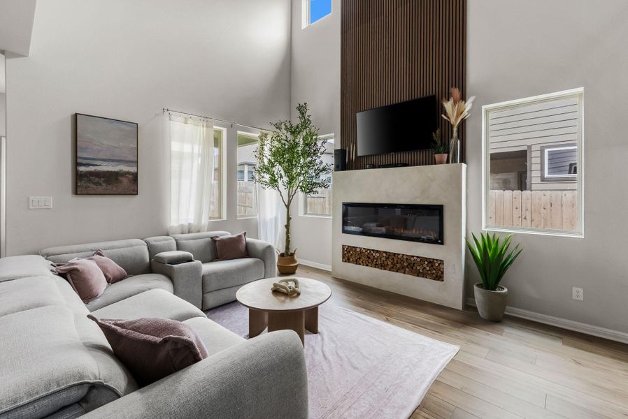 Living room featuring a high ceiling, light wood-style flooring, and a glass covered fireplace