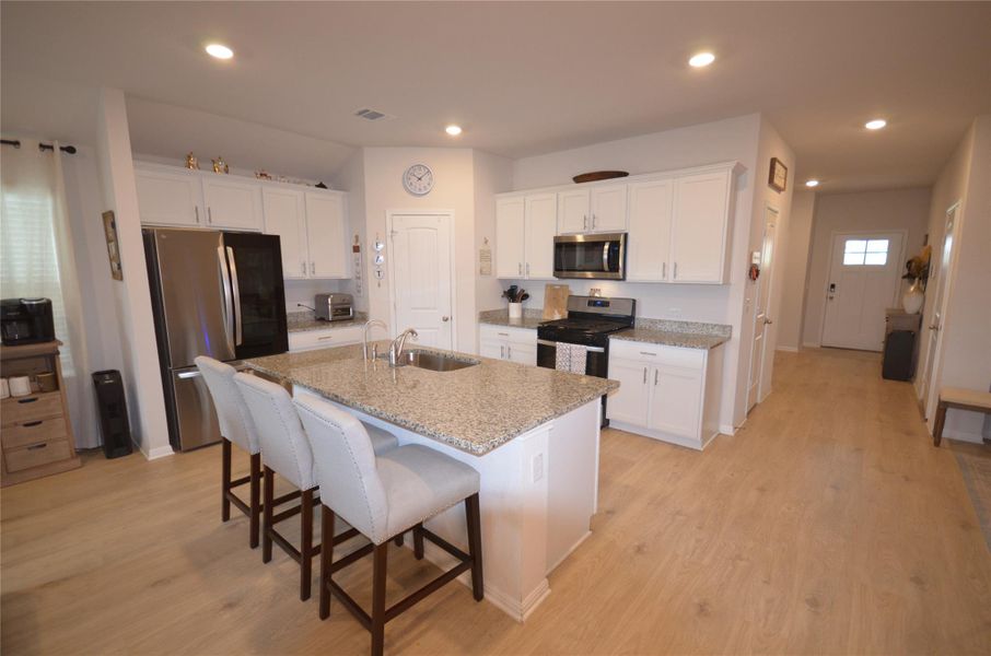 Kitchen featuring appliances with stainless steel finishes, a kitchen breakfast bar, white cabinets, a center island with sink, and light wood-style flooring Kitchen featuring appliances with stainless steel finishes, a kitchen breakfast bar, white cabinets, a center island with sink, and light wood-style flooring