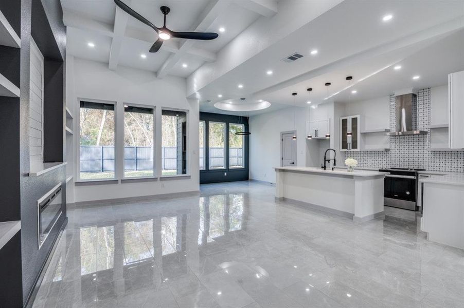 Kitchen featuring stainless steel range, wall chimney range hood, decorative light fixtures, white cabinetry, and an island with sink