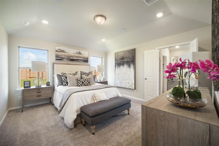 Escape and relax in the exquisite primary suite, a haven to unwind after a long day. The spacious room, located on first floor, boasts plush carpeting, soothing paint tones, high ceilings, and expansive windows adorned with privacy blinds. Sample photo of completed home with similar floor plan. Actual colors and selections may vary.