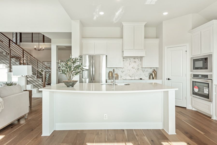 Open kitchen with large white island, white cabinets, marble backsplash, and stainless steel appliances on hardwood floors