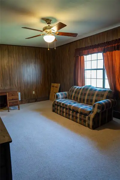 Living area featuring carpet flooring, a ceiling fan, and wood walls