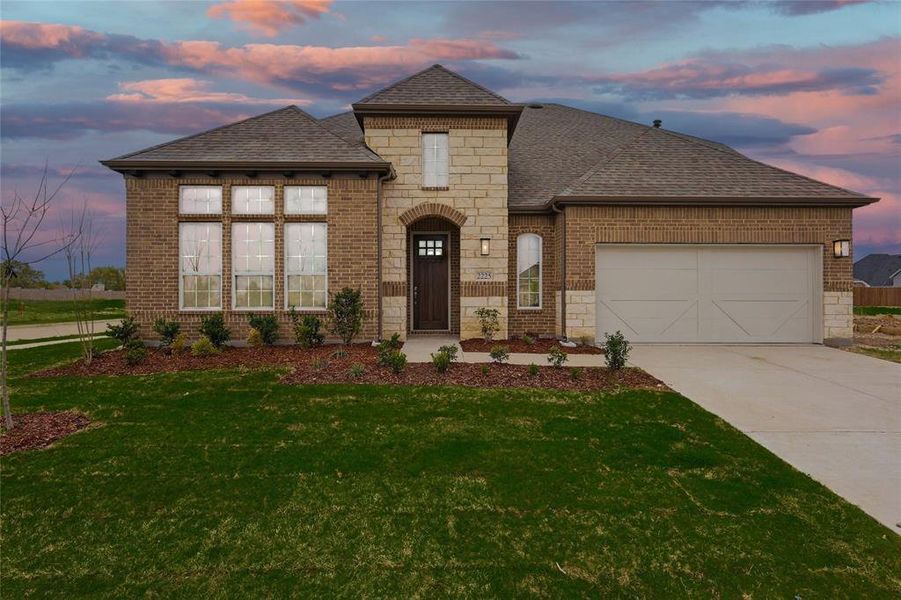 French country style house featuring stone siding, roof with shingles, brick siding, and concrete driveway