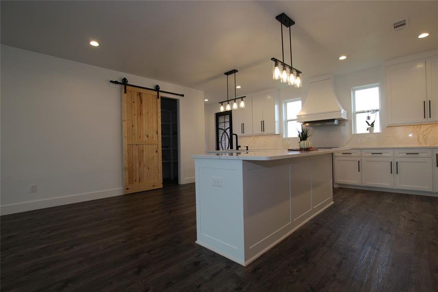 Kitchen featuring a barn door, tasteful backsplash, white cabinetry, custom range hood, and recessed lighting Kitchen featuring a barn door, tasteful backsplash, white cabinetry, custom range hood, and recessed lighting