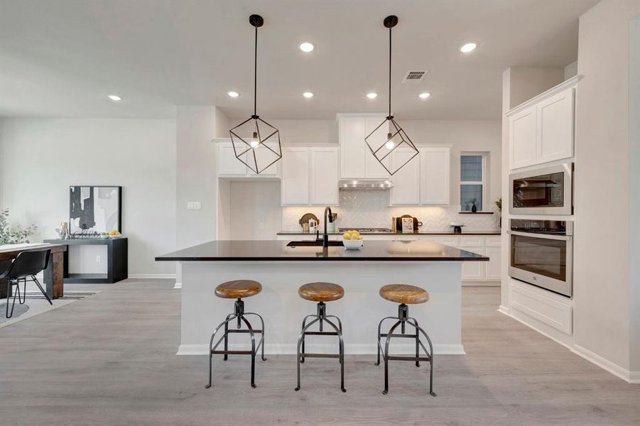 Open-concept kitchen with a large island featuring a dark countertop and pendant lighting