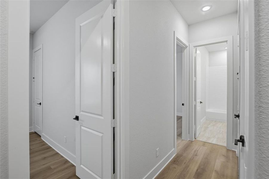 Hallway with light wood finished floors, a textured wall, and recessed lighting