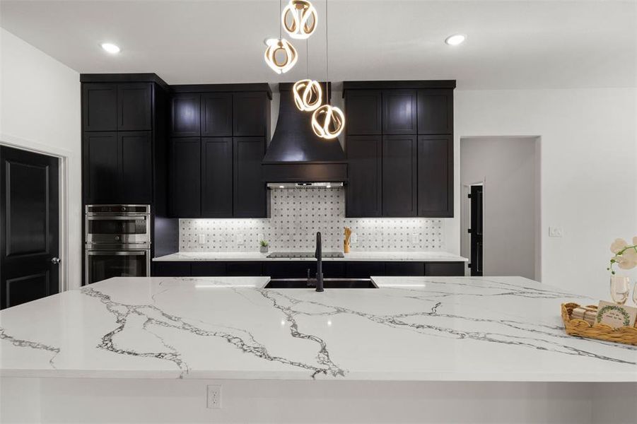 Kitchen with dark cabinets, light stone countertops, backsplash, and recessed lighting
