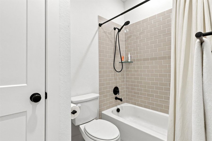 A modern shower and tub combination boasts classic subway tile surrounds and dark hardware accents.