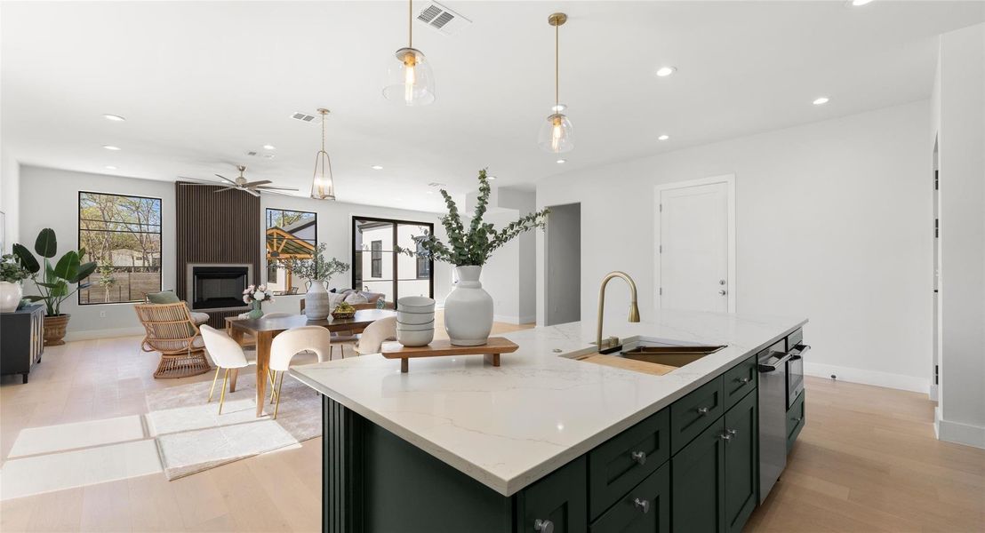 Kitchen with light stone countertops, green cabinetry, light wood-type flooring, a kitchen island with sink, and open floor plan