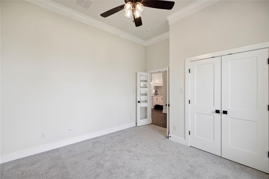 Unfurnished bedroom featuring a closet, ceiling fan, crown molding, light colored carpet, and a towering ceiling