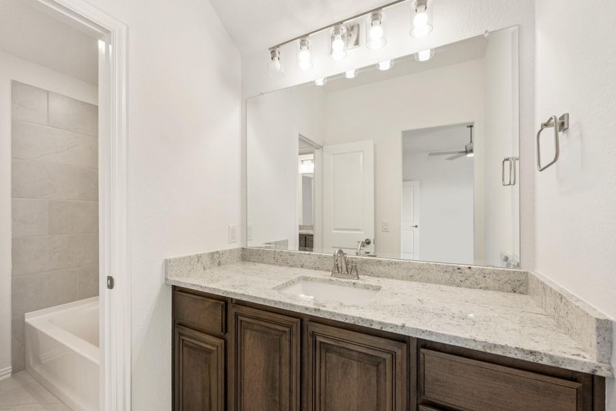 Bathroom with dark wood vanity, granite countertop, large mirror, and tiled soaking tub in background Bathroom with dark wood vanity, granite countertop, large mirror, and tiled soaking tub in background