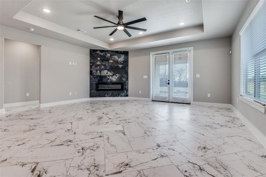 Unfurnished living room featuring a tray ceiling, a high end fireplace, ceiling fan, light marble finish floors, and french doors
