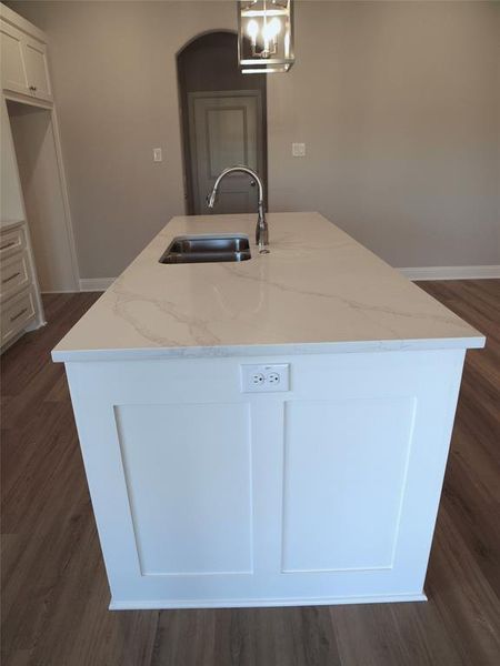 Kitchen with hanging light fixtures, an island with sink, white cabinetry, and sink