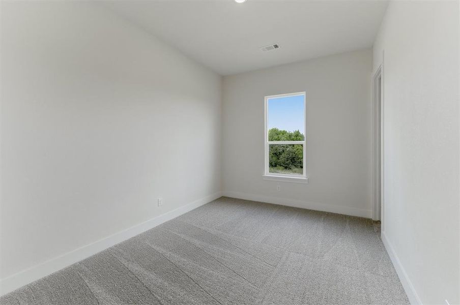 Bright interior room featuring a large window with white trim, light gray patterned carpeting, and fresh white walls