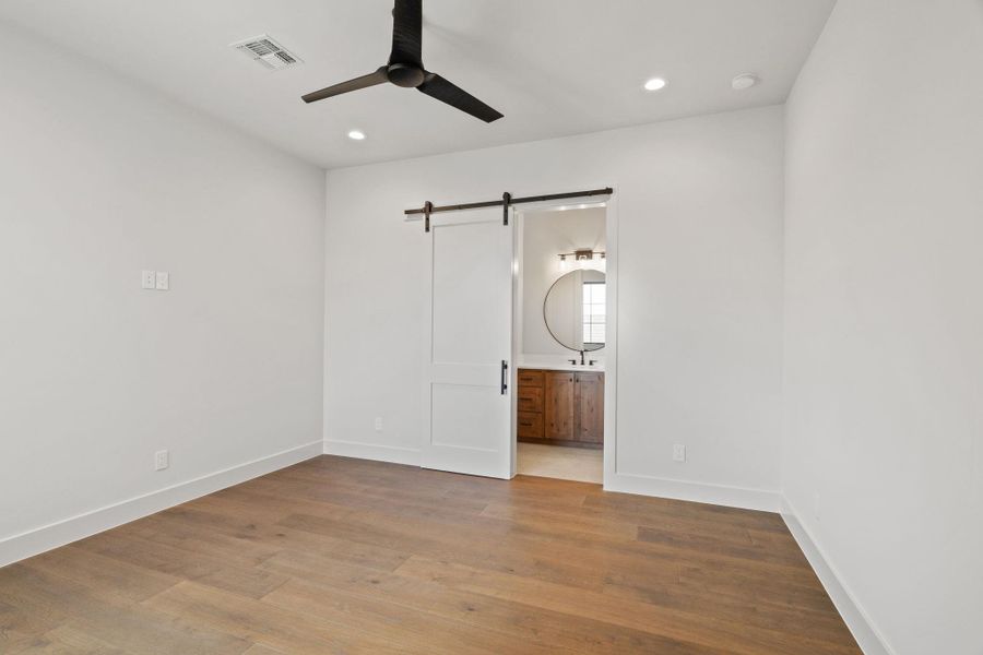 1 of 3 bedrooms upstairs with a barn door, wood finished floors, a ceiling fan, Hollywood bath.