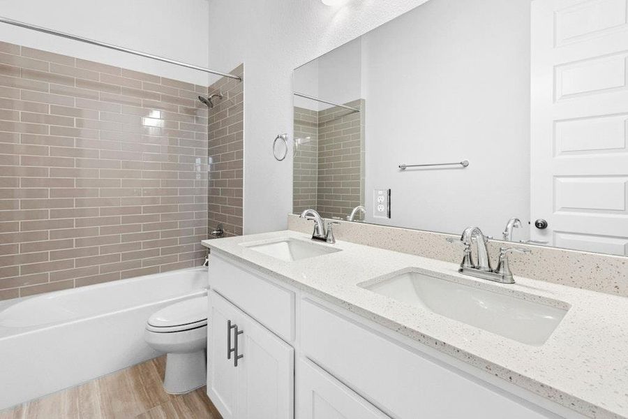 Full bath with double vanity, light wood-style floors, and shower / tub combination