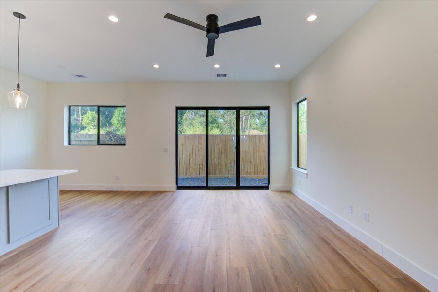 Spacious and bright living area featuring sleek vinyl plank floors, modern recessed lighting, and large windows offering serene outdoor views. Perfect for relaxation and entertaining. Spacious and bright living area featuring sleek vinyl plank floors, modern recessed lighting, and large windows offering serene outdoor views. Perfect for relaxation and entertaining.