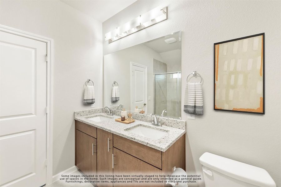 Bathroom with double sink vanity, wood cabinets, granite countertop, large mirror, and walk-in shower visible in background.