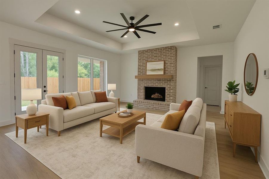 Living room featuring a brick fireplace, a raised ceiling, light wood-type flooring, a ceiling fan, and recessed lighting