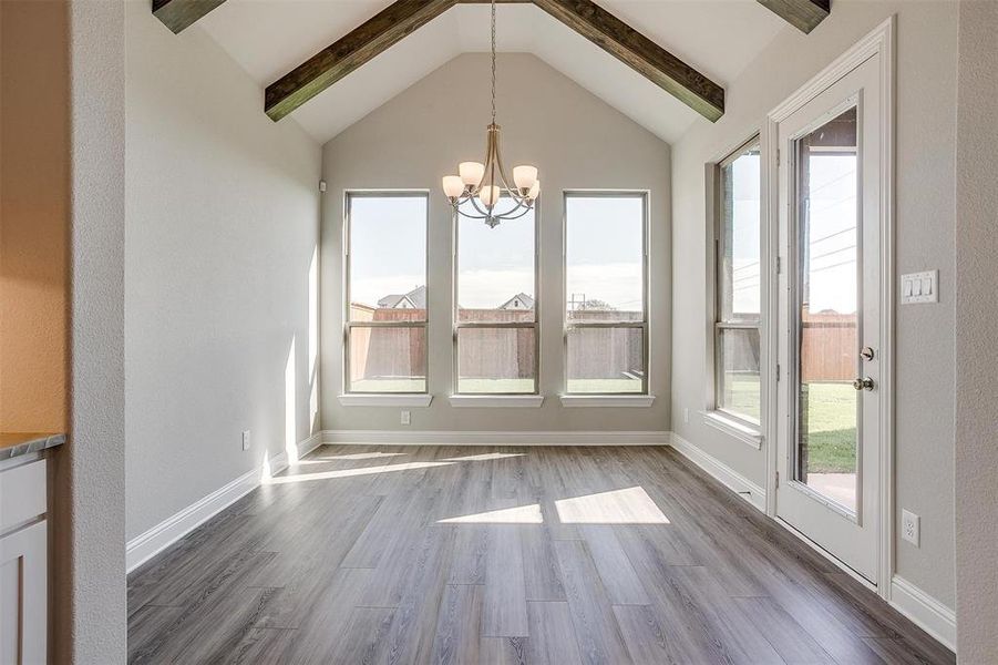 Unfurnished dining area with a chandelier, wood-type flooring, vaulted ceiling with beams, and a healthy amount of sunlight